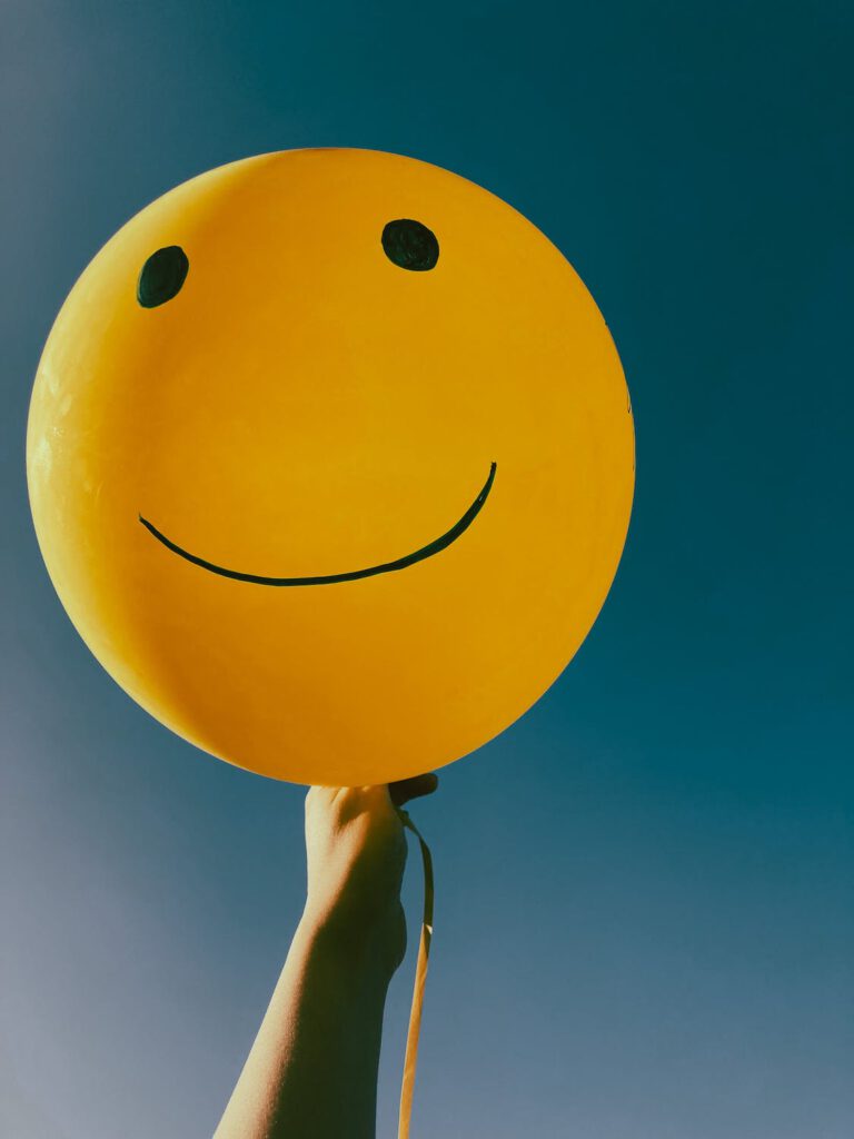 Hand die gele ballon vasthoudt met daarop een smiley.